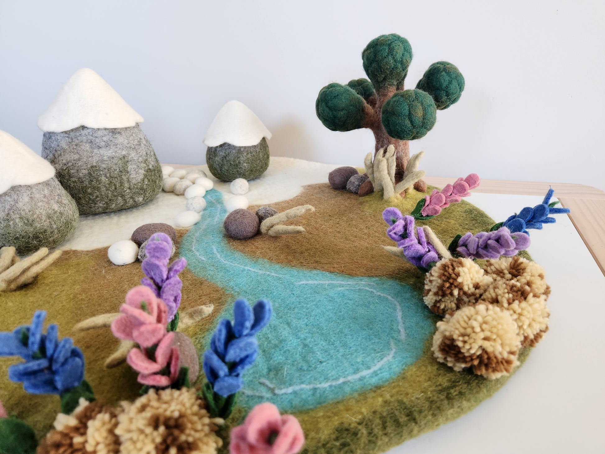 Handmade felt landscape with tree, flowers, and a river on a white background