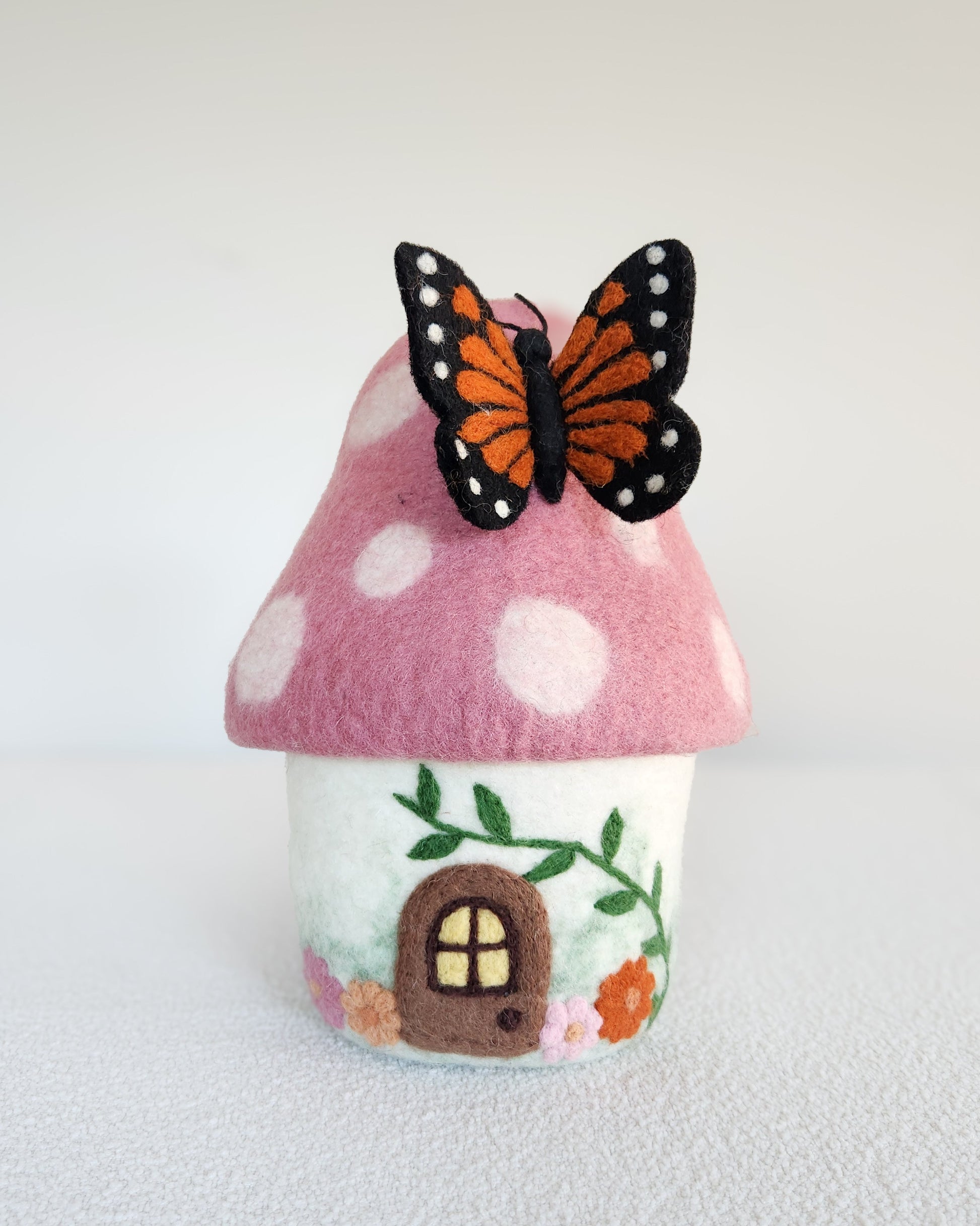 Felt mushroom house with a butterfly on a white background