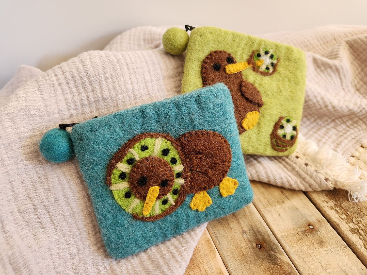 FELT KIWI COIN PURSES. BLUE KIWI PURSE WITH KIWI BIRD AND KIWI SLICE OVER HEAD. GREEN KIWI PURSE WITH KIWI BIRD WITH KIWI SLICE STUCK ON BEAK.